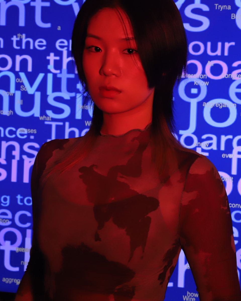 Chen Wang, lit in red, in front of a wall of projected blue text.