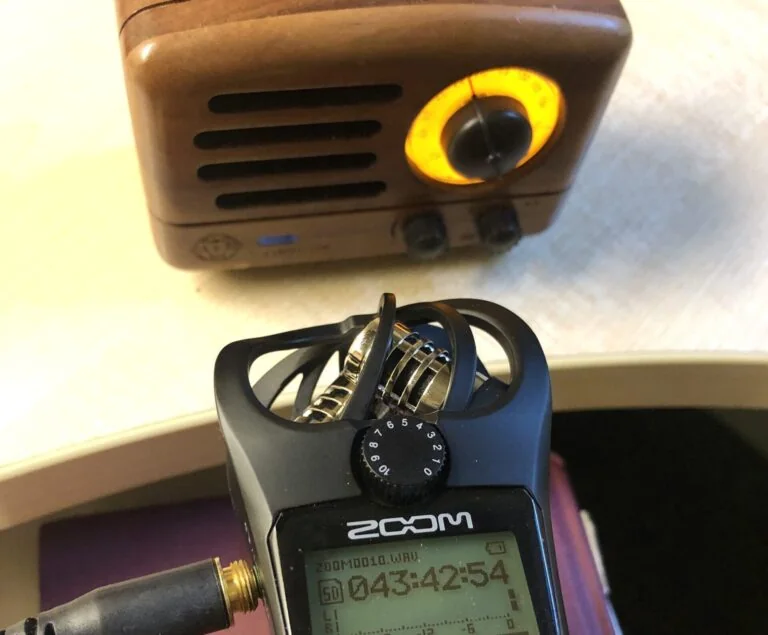 A handheld Zoom recorder capturing sound played back through a small vintage radio speaker