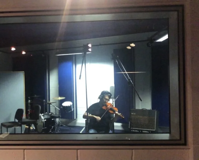 Violinist recording in the live room, seen through the control-room window