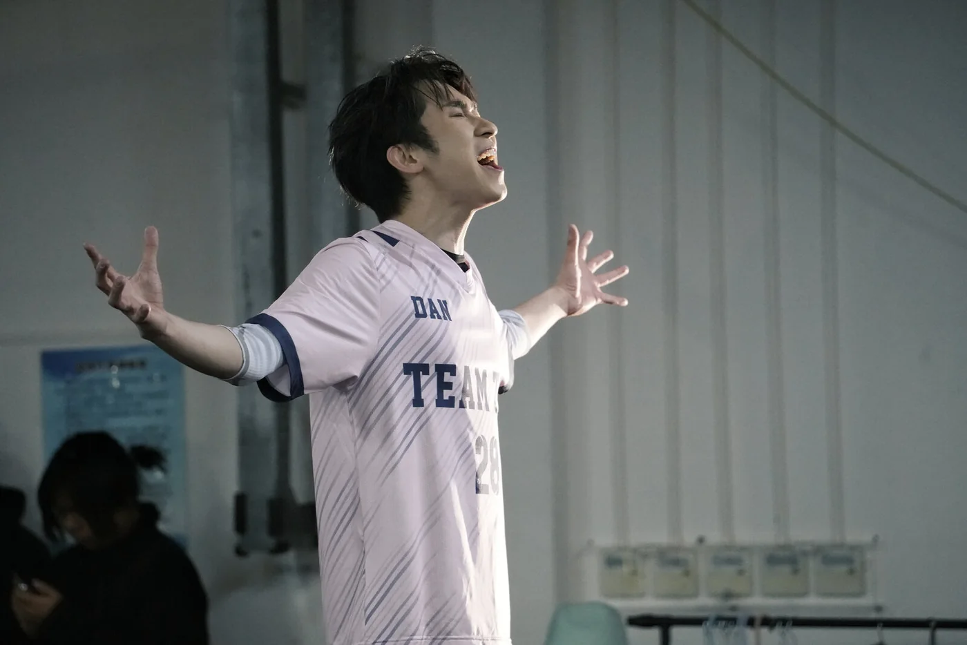 Reincarnated as a Convenience Store: a performer in a white sports jersey singing with arms spread wide