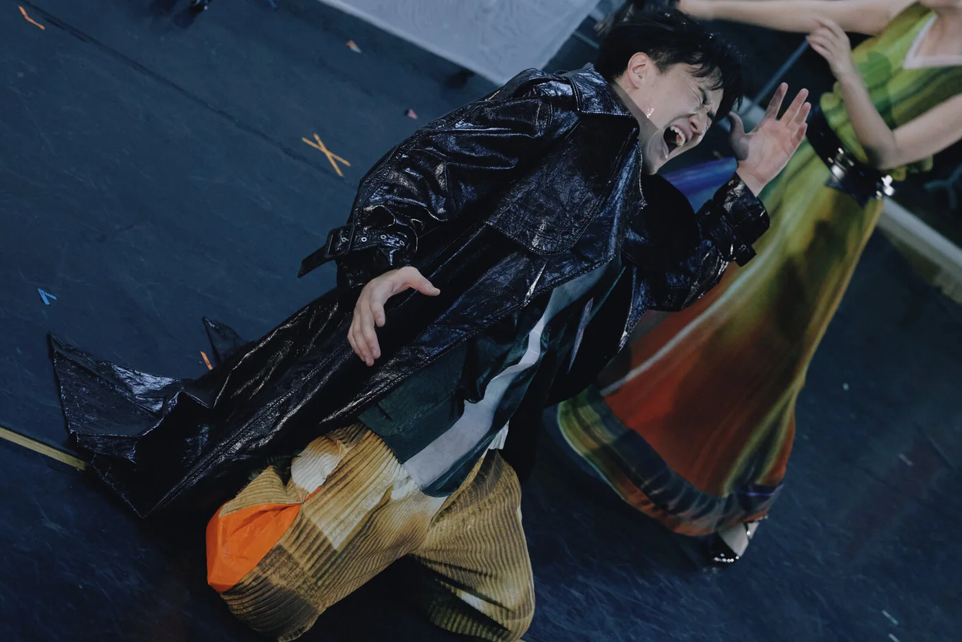 Reincarnated as a Convenience Store: a performer in a glossy black coat in an expressive pose