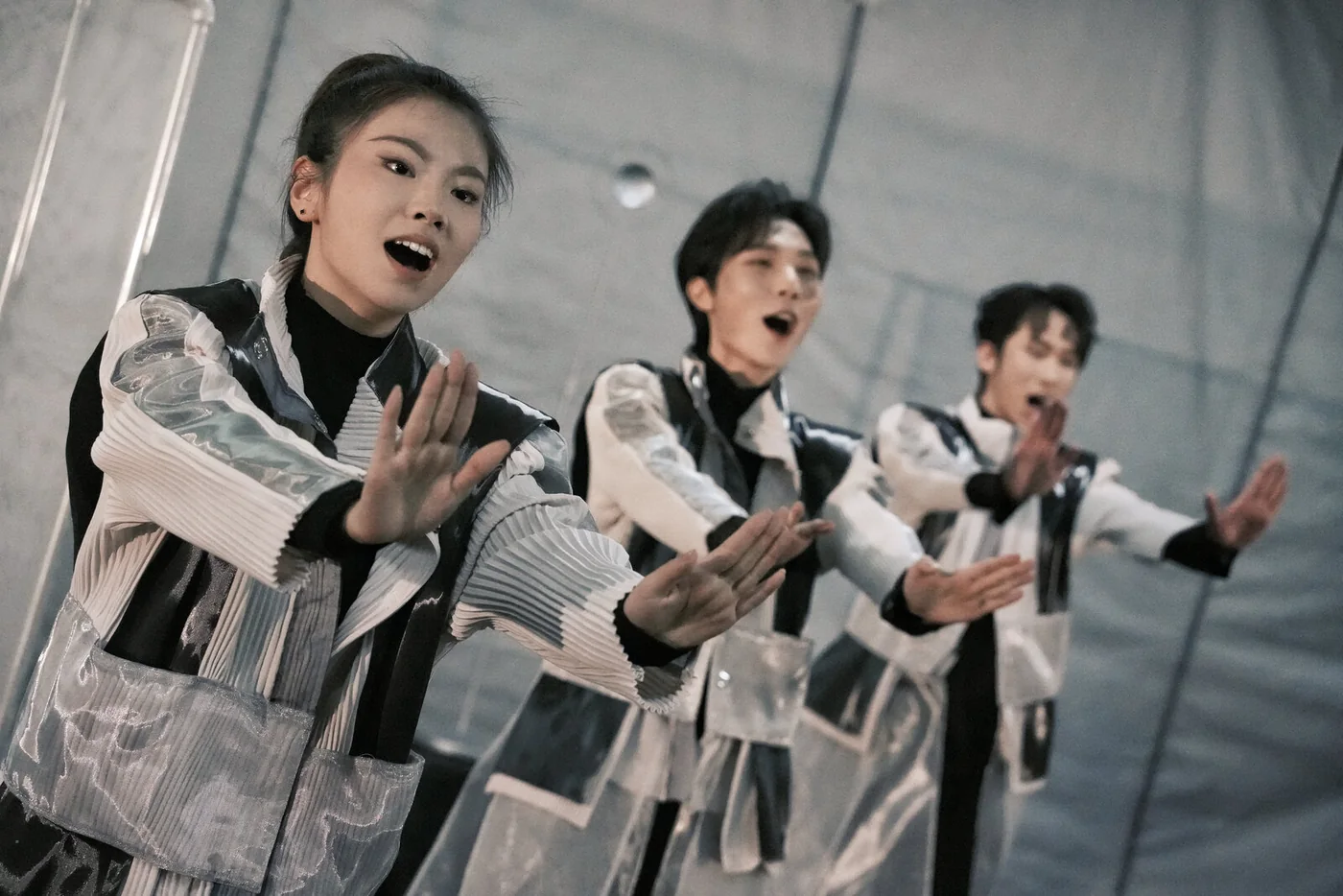 Reincarnated as a Convenience Store: three performers in pleated costumes singing with outstretched arms