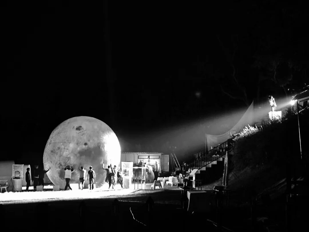 The Moon, The Moon: black-and-white photograph of the moon set and performers in an outdoor courtyard